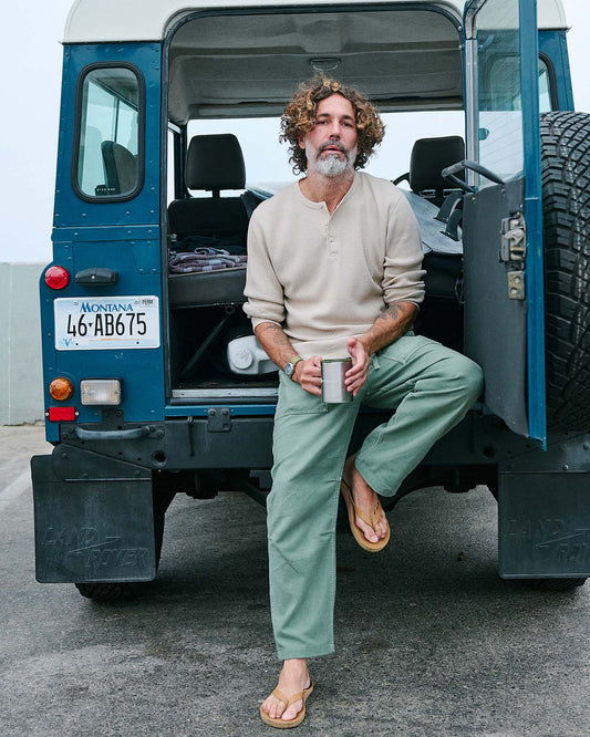Man sitting in the open door of a blue vehicle holding a mug, with 'Montana' license plate visible.