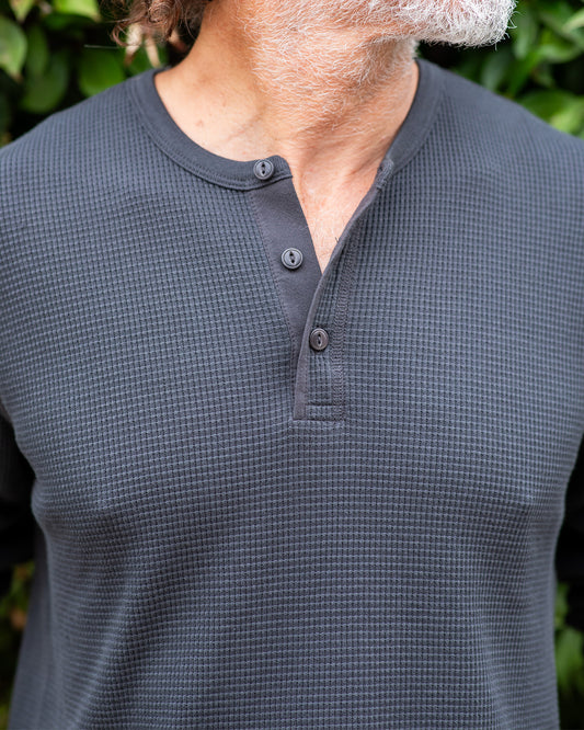 Person wearing a black textured long-sleeve shirt with buttons against a blurred green background