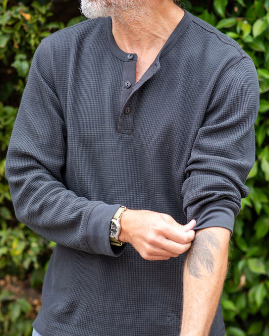 Man wearing a black long-sleeve shirt against a green leafy background