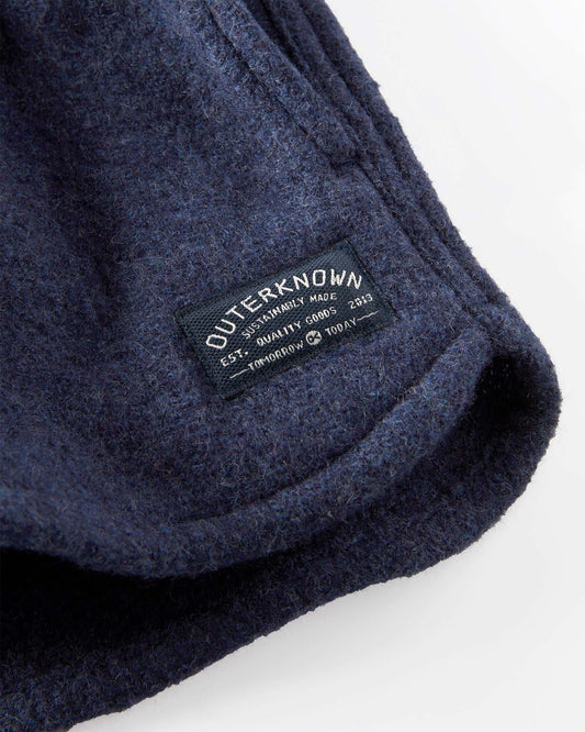 Closeup of a navy blue jacket with 'Outerknown' brand label on a white background