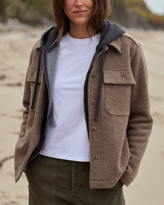 Person wearing a brown jacket with a hood on a beach