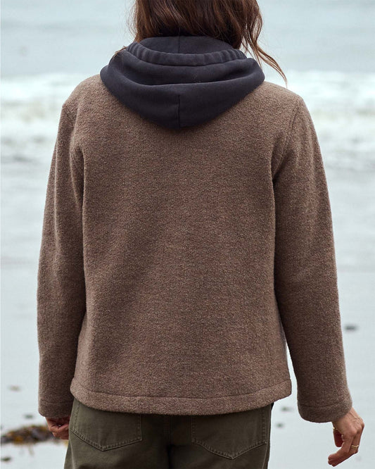 Person wearing a brown jacket with a hood standing on a beach landscape