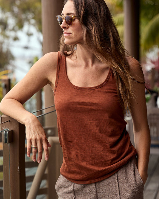 Woman wearing a rust-colored tank top and sunglasses, standing outdoors.
