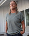 Woman wearing a greyish-green t-shirt standing outdoors with a neutral background