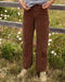 Person wearing brown corduroy pants standing in a field with white flowers and a wooden fence.
