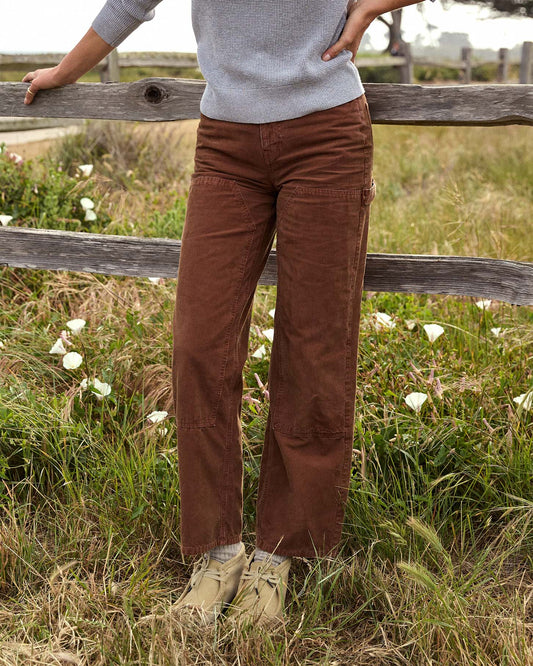 Person wearing brown pants standing in a grassy field with a wooden fence.
