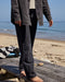 Person wearing dark pants and a jacket on a beach with ocean in the background