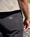 Person wearing dark gray pants with a brand logo on the back pocket, standing outdoors.