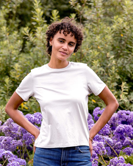 Person wearing a light grey t-shirt and blue jeans standing in front of purple flowers and green foliage