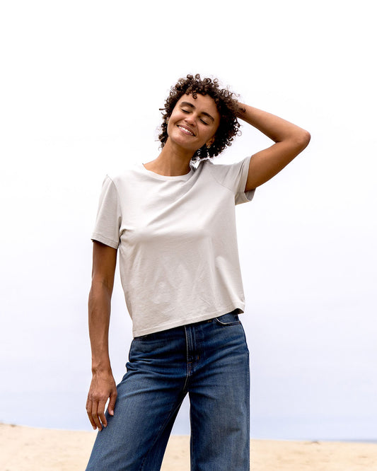 Woman wearing a light grey t-shirt and blue jeans against a clear sky.