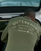 Person wearing a green sweatshirt with 'Outerknown' branding, opening a car trunk.