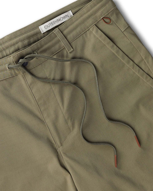 Close-up of olive green pants with drawstring and 'Outerknown' brand label.