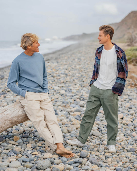 Two people standing on a pebbly beach with a scenic background