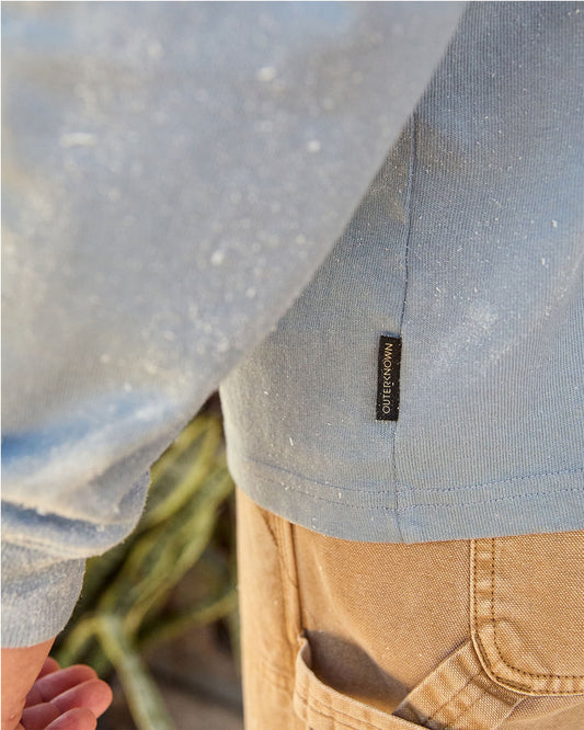 Close-up of a person wearing a light blue shirt with a visible brand logo, standing outdoors.