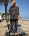 Person standing on a wooden bench at a beach with palm trees and ocean in the background