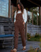 Woman wearing brown overalls standing on a wooden deck.