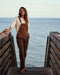 Woman in brown overalls standing on a wooden dock by the ocean