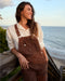 Woman wearing brown overalls standing by a body of water