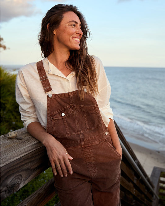 Woman wearing brown overalls standing by a body of water