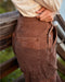Brown corduroy pants with a visible brand logo worn by a person against a blurred natural background.