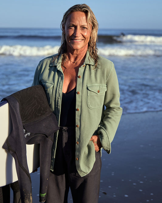 A woman wearing a green blanket shirt on the beach with ocean waves in the background