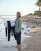 A woman wearing a green blanket shirt on the beach with ocean waves in the background