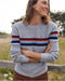 Woman wearing a gray sweater with colorful stripes standing outdoors.