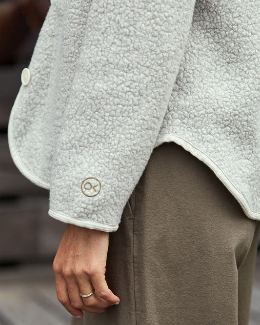 Close-up of a person wearing a textured light gray wool jacket with a brand logo.