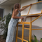 Woman standing on a ladder cleaning a window outside a house