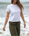 Person wearing a white t-shirt and green pants standing on a beach.