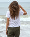 Person wearing a white t-shirt and green pants standing on a beach.